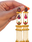 Pair of gold-plated ruby glass tassel jhumkas held in hand against white background