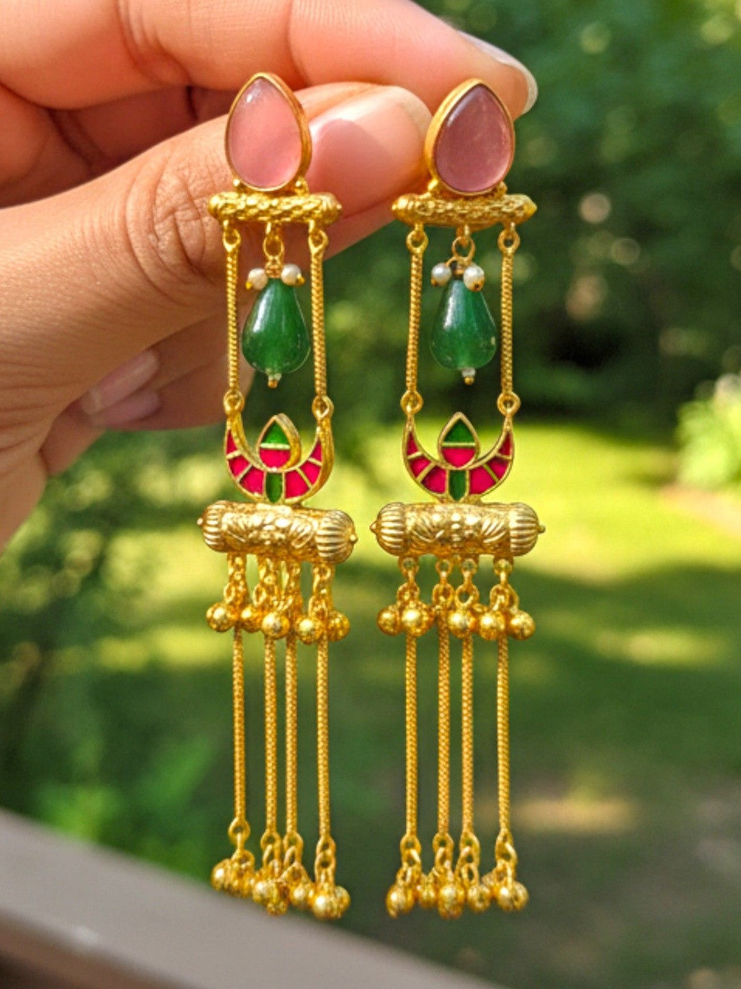 Both tassel jhumka earrings held in hand showing pink stone, green bead, meenakari crescent and ghungroo tassels