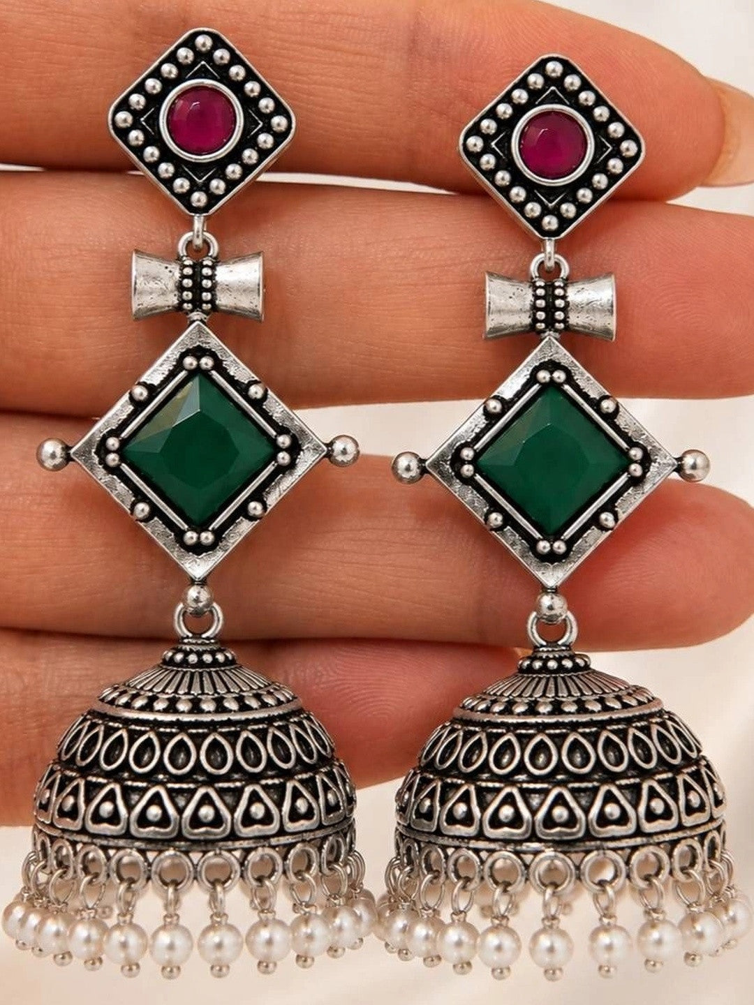 Close-up of oxidised silver jhumka earring pair held on a hand showing engraved dome and pearl fringe detail