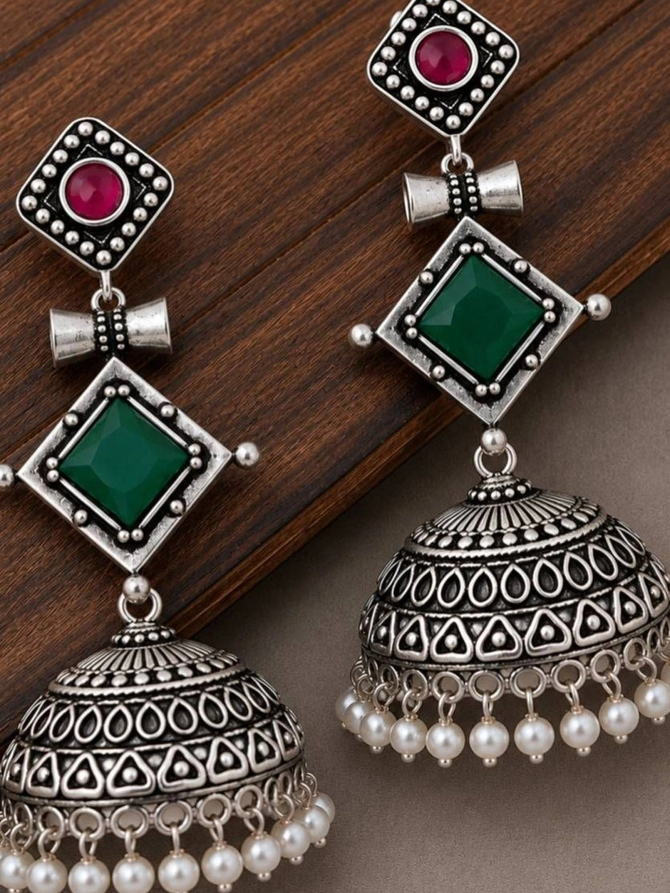 Two oxidised silver jhumka earrings displayed on a wooden surface showing full geometric layered design