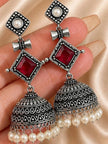 Close-up of two geometric jhumka earrings held in a hand showing engraved dome detail and red stone