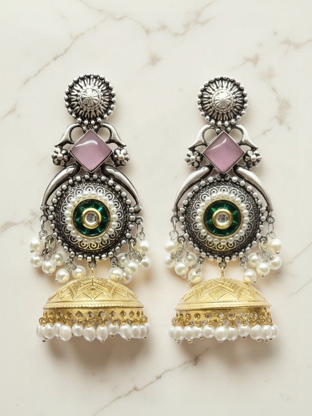 Pair of oxidised silver kundan jhumka earrings with pink stone, pearl drops, and gold-tone bell on marble background
