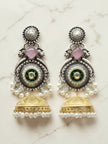 Pair of oxidised silver kundan jhumka earrings with pink stone, pearl drops, and gold-tone bell on marble background
