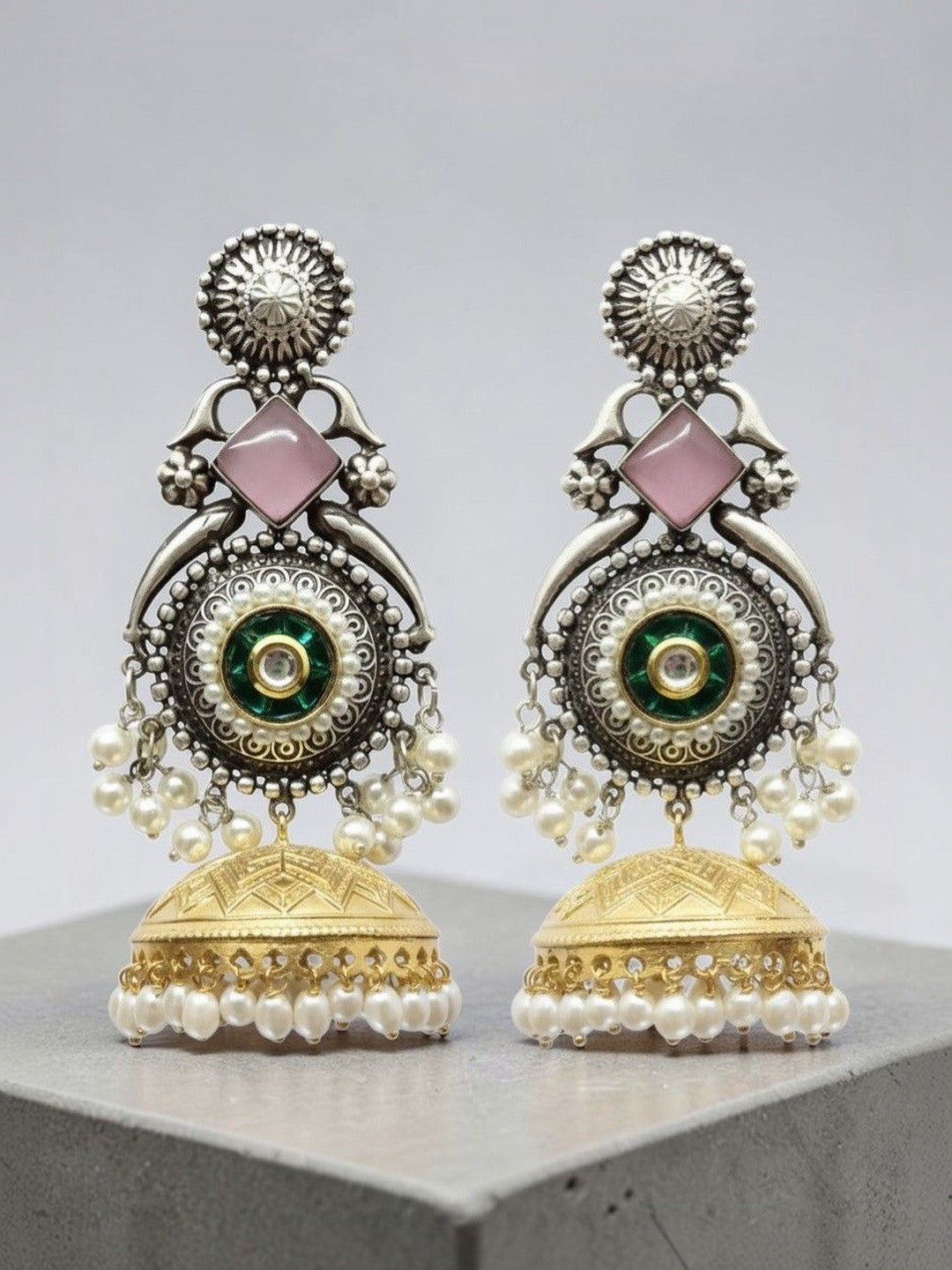 Front-facing oxidised silver peacock jhumka earrings with green kundan centre and pearl bead fringe on grey surface