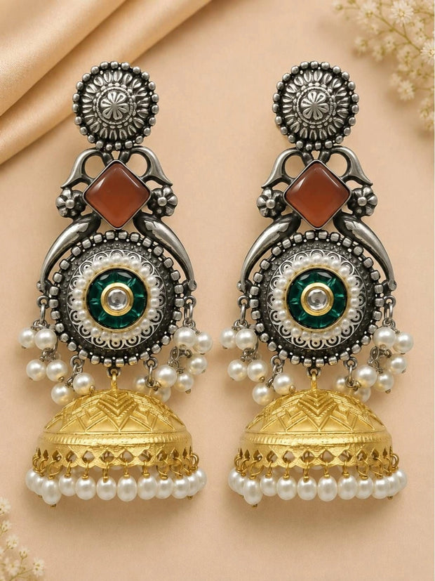 Pair of dual-tone jhumka earrings with oxidised silver upper, green kundan centre, pearl fringe and gold dome bell, laid flat