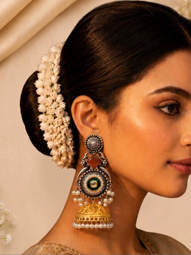 Model wearing large oxidised silver and gold jhumka earring with pearl drops and white flower hair accessory