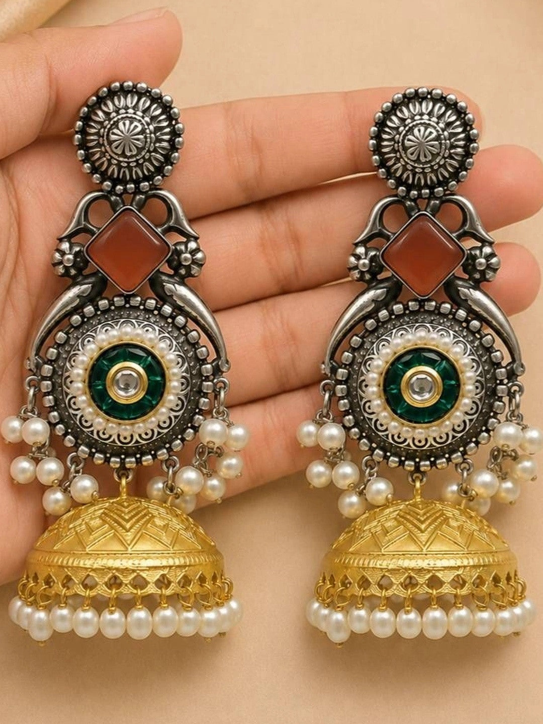 Two jhumka earrings resting on a palm showing peacock motif, carnelian stone, pearl-ringed kundan centre and gold bell