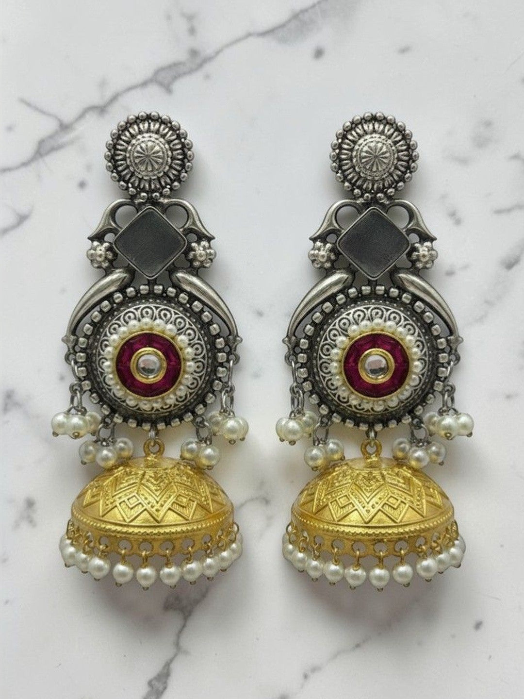 Pair of oxidised dual-tone kundan jhumka earrings with pearl drops on a white marble surface