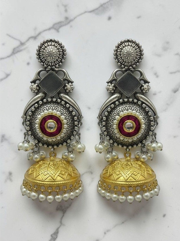 Pair of oxidised dual-tone kundan jhumka earrings with pearl drops on a white marble surface