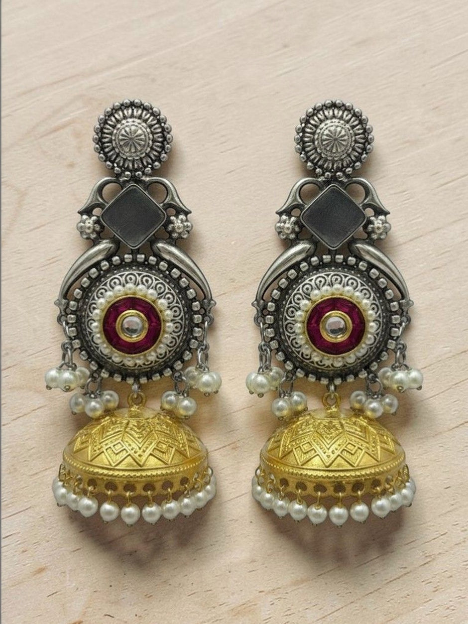 Oxidised silver and gold-tone jhumka earrings with red enamel kundan centre displayed on a wooden surface