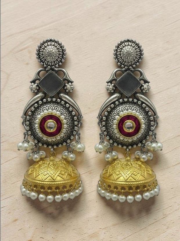 Oxidised silver and gold-tone jhumka earrings with red enamel kundan centre displayed on a wooden surface