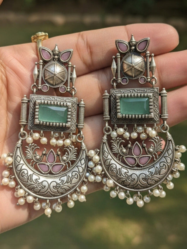 Both oxidised silver chandbali earrings held in a woman's palm showing engraved lotus and pearl drop details