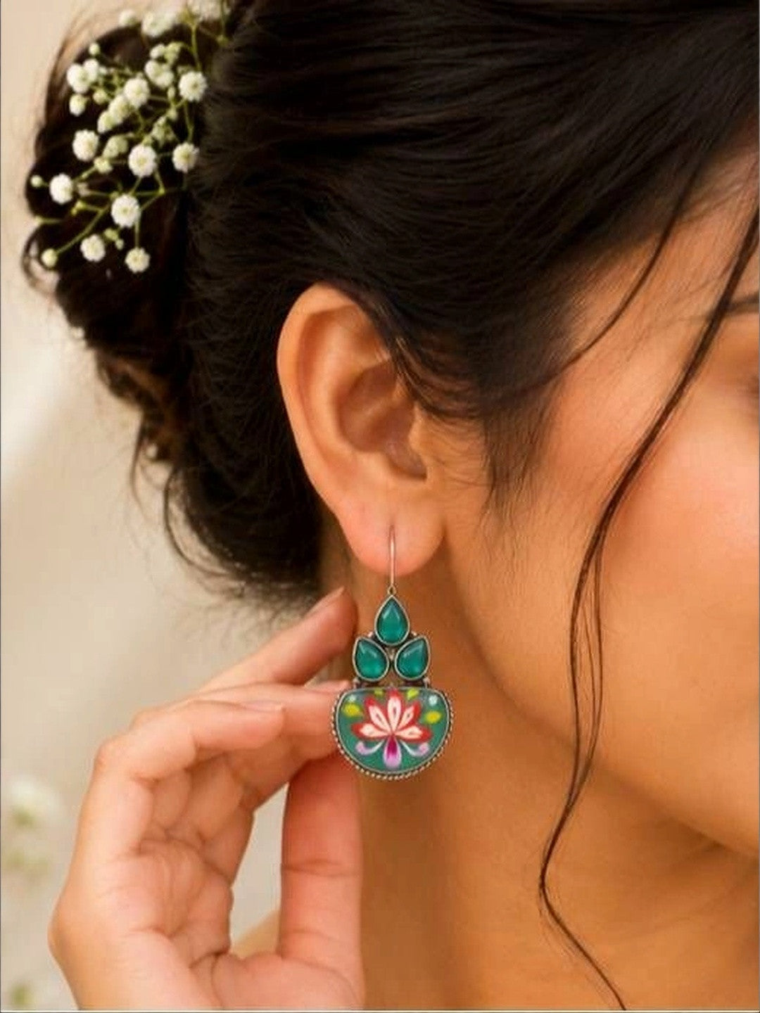 Woman wearing oxidised silver meenakari earring with green stones, hair styled in a bun with baby's breath flowers