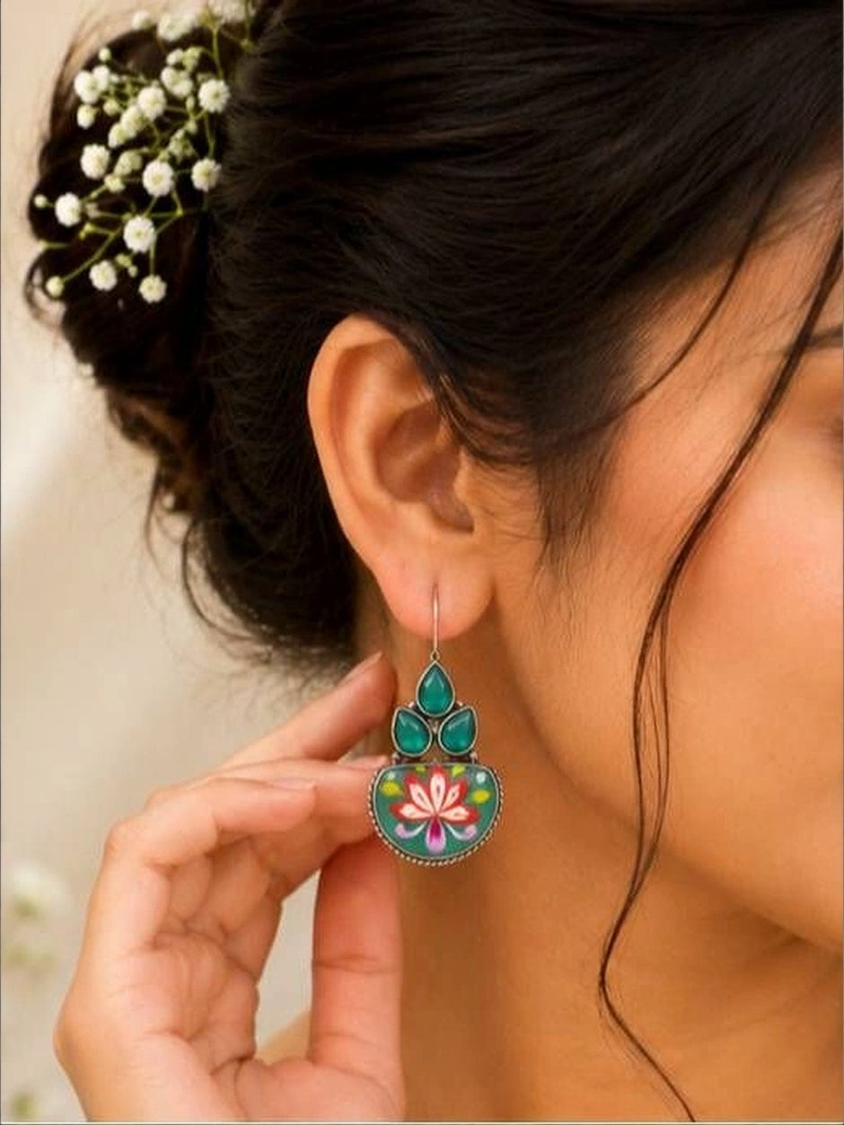Woman wearing oxidised silver meenakari earring with green stones, hair styled in a bun with baby's breath flowers