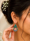 Woman wearing oxidised silver meenakari earring with green stones, hair styled in a bun with baby's breath flowers