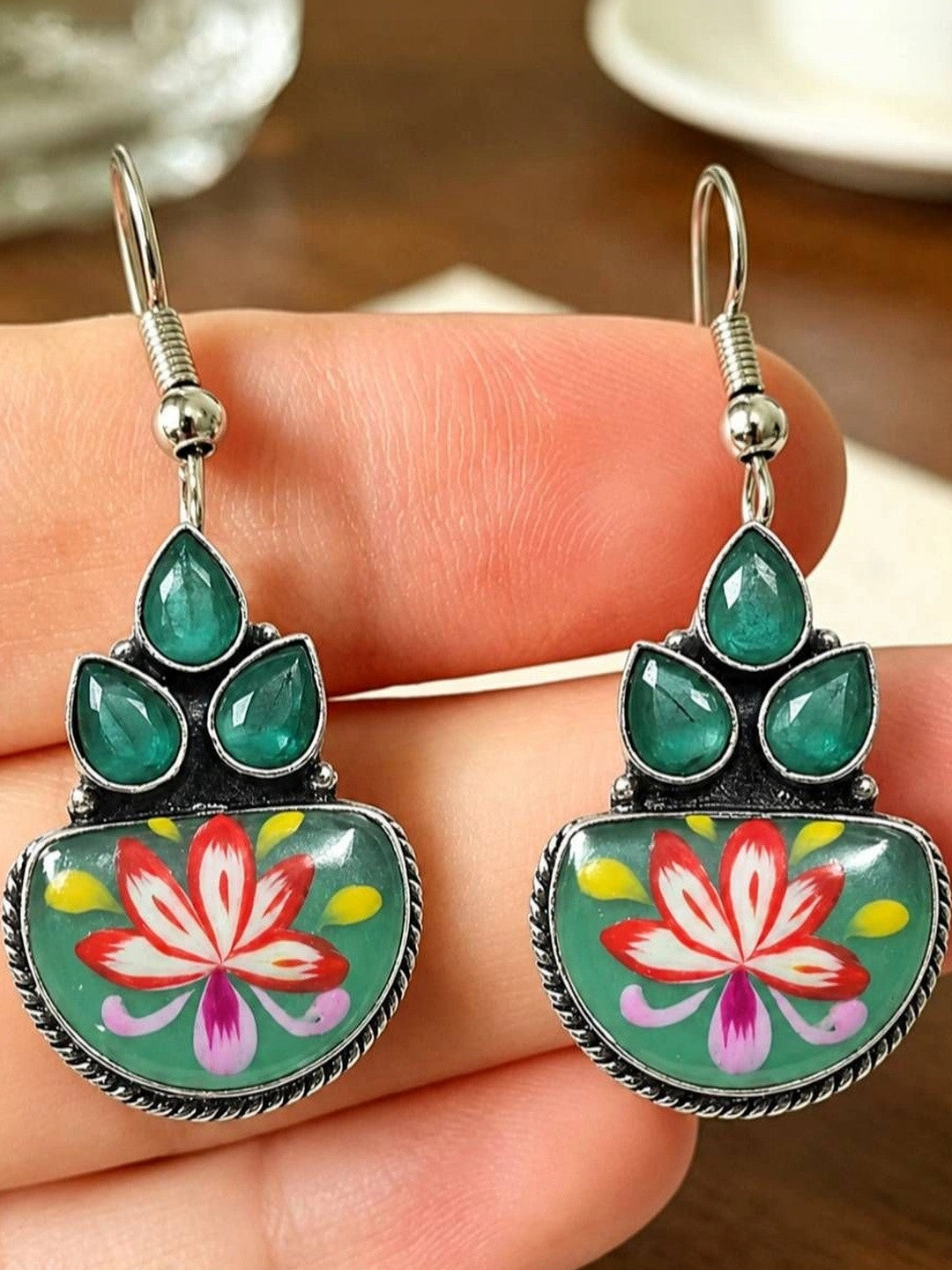 Close-up of both meenakari hook earrings resting on a hand, showing vivid red, pink and yellow lotus enamel detail