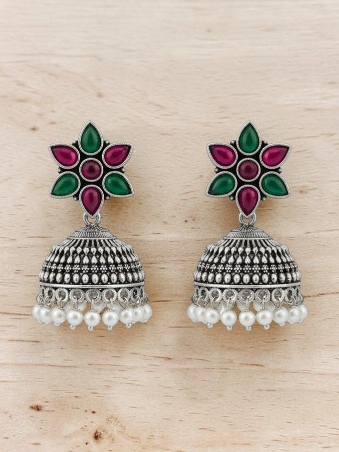 Pair of oxidised silver jhumka earrings with pink green flower stud and white pearl drops on wooden surface