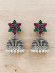 Pair of oxidised silver jhumka earrings with pink green flower stud and white pearl drops on wooden surface
