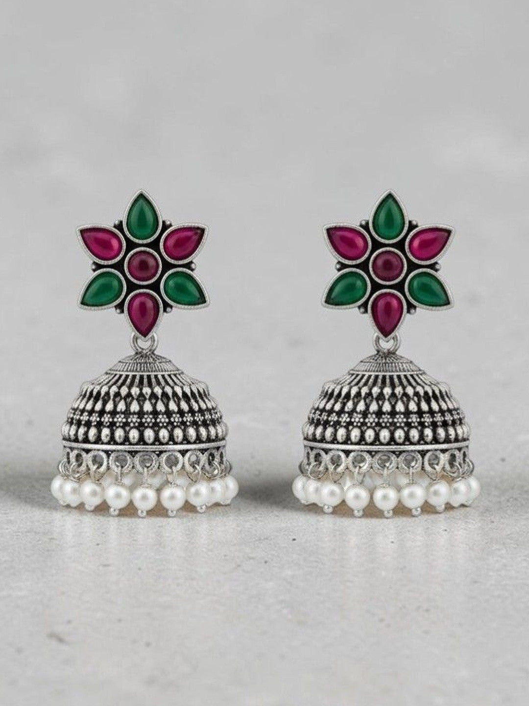 Front view of oxidised silver jhumka earrings showing floral resin top and pearl fringe on grey background