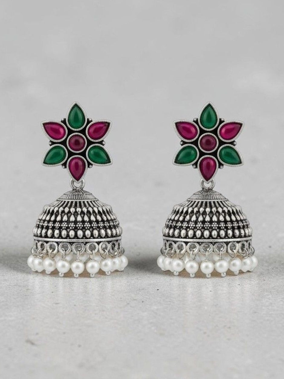Front view of oxidised silver jhumka earrings showing floral resin top and pearl fringe on grey background