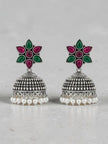 Front view of oxidised silver jhumka earrings showing floral resin top and pearl fringe on grey background