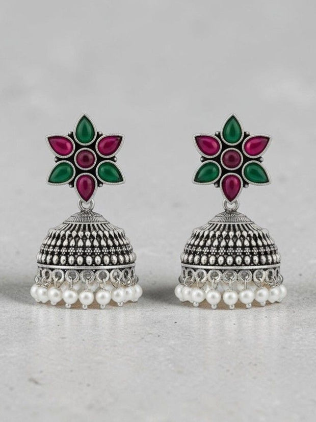 Front view of oxidised silver jhumka earrings showing floral resin top and pearl fringe on grey background