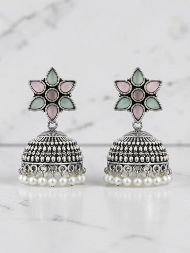 Pair of oxidised silver jhumka earrings with mint and blush flower studs and faux-pearl drops on marble background