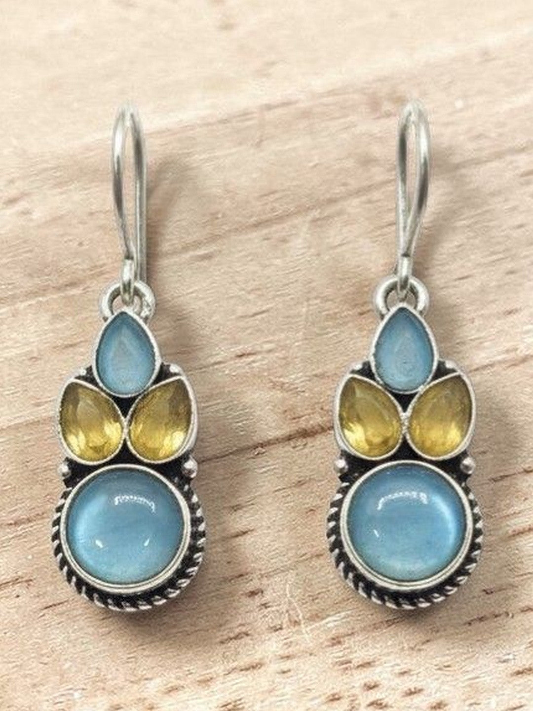 Pair of oxidised silver drop earrings with blue round cabochon and yellow teardrop stones on a wooden surface