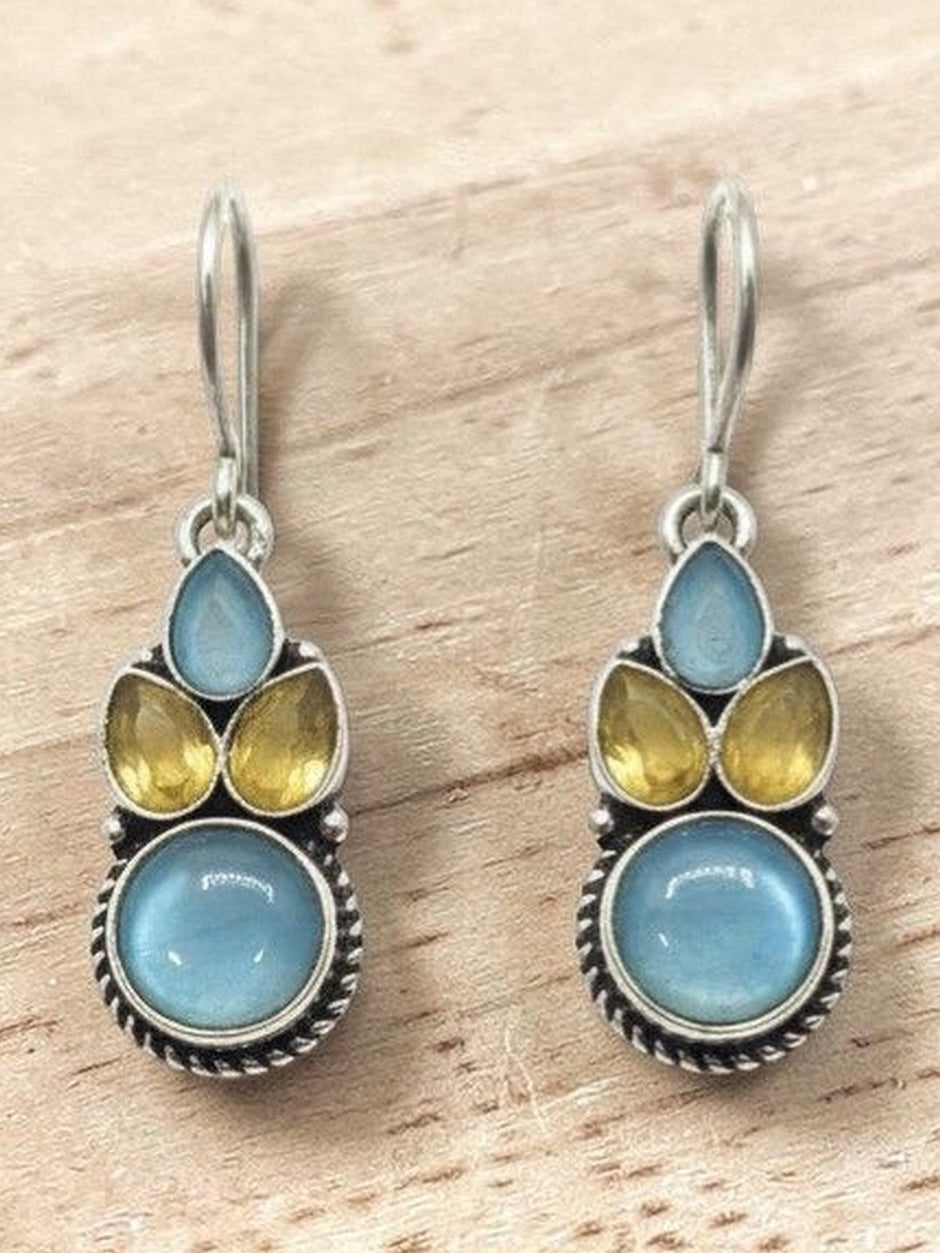 Pair of oxidised silver drop earrings with blue round cabochon and yellow teardrop stones on a wooden surface