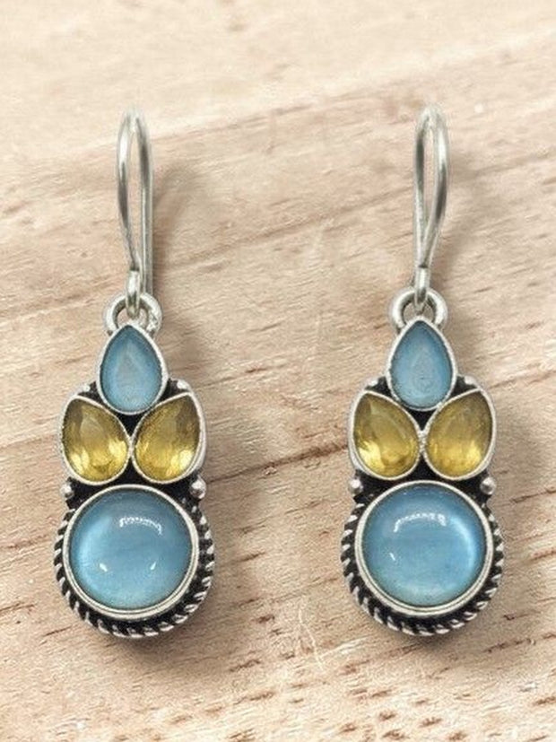 Pair of oxidised silver drop earrings with blue round cabochon and yellow teardrop stones on a wooden surface