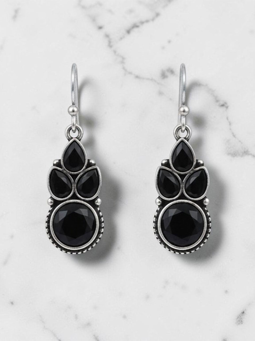 Pair of oxidised silver drop earrings with black pear and round stones on white marble background