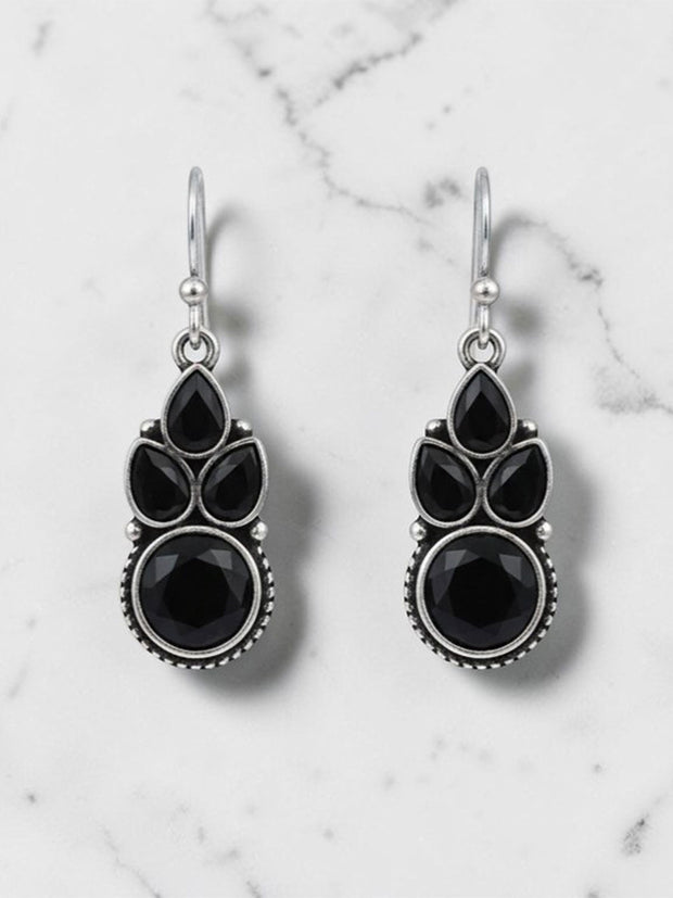 Pair of oxidised silver drop earrings with black pear and round stones on white marble background