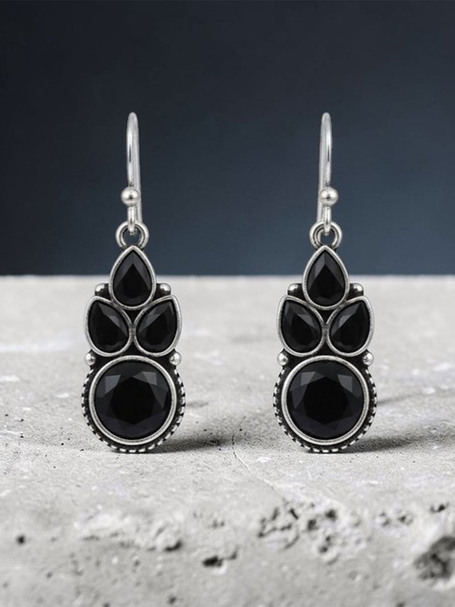 Oxidised silver black stone dangle earrings standing upright on grey textured concrete surface