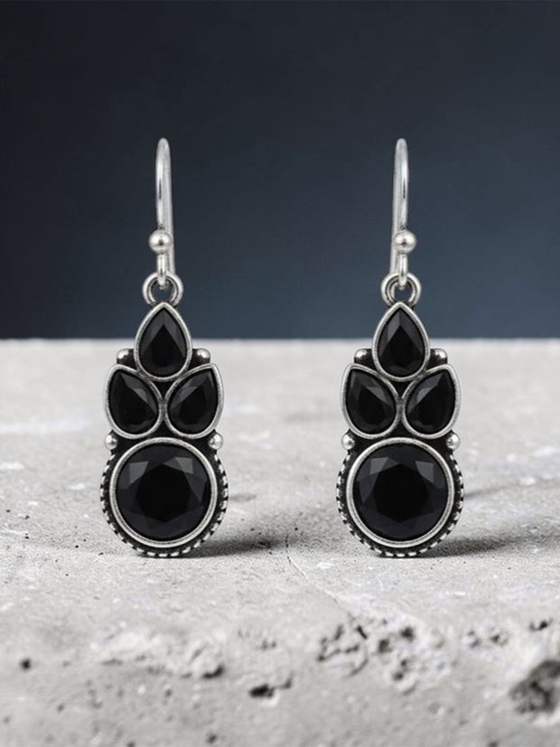 Oxidised silver black stone dangle earrings standing upright on grey textured concrete surface