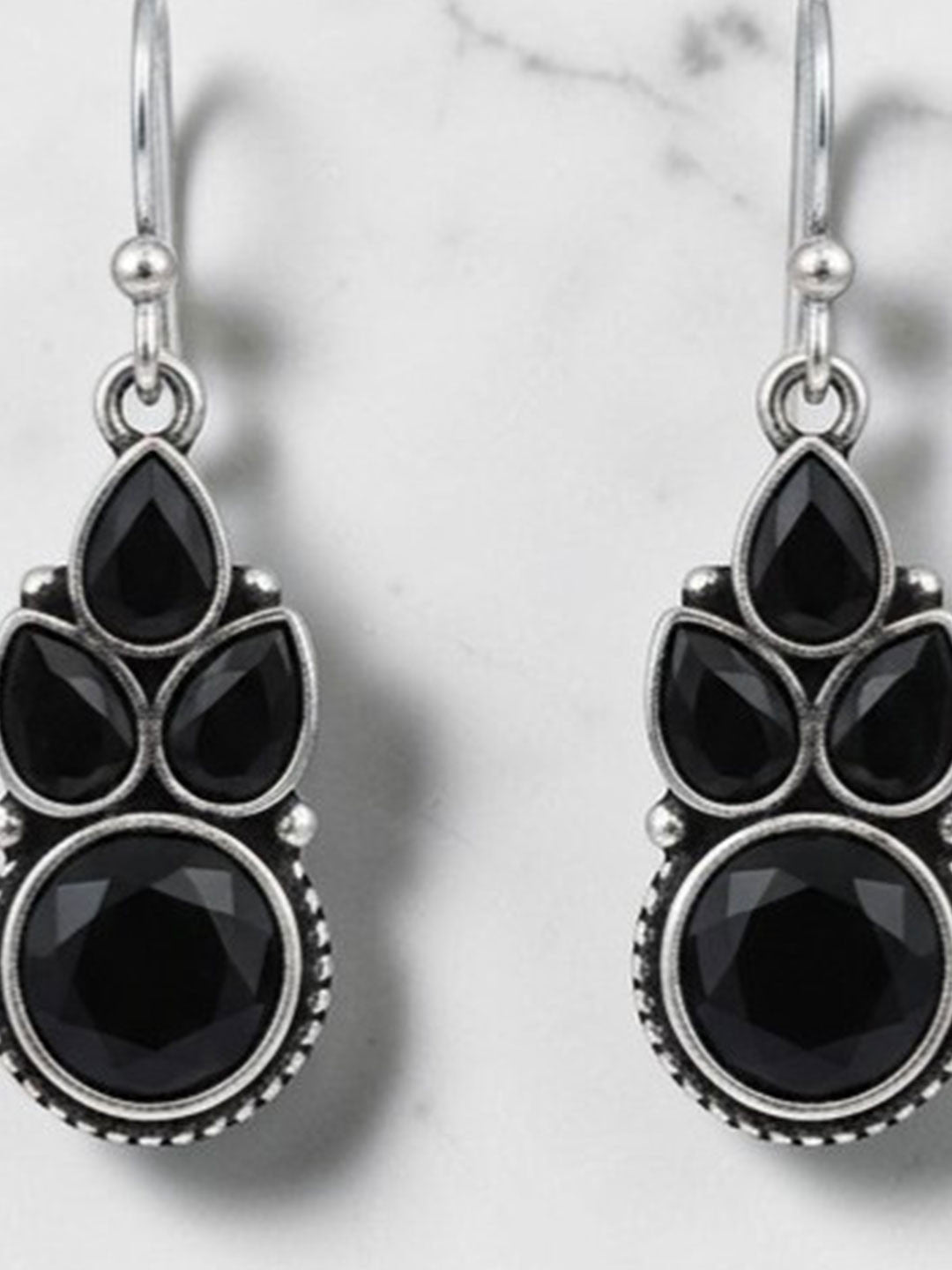 Close-up of black faceted stone cluster earrings with oxidised silver detailing on marble