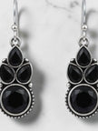 Close-up of black faceted stone cluster earrings with oxidised silver detailing on marble