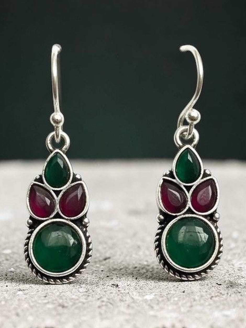 Close-up of oxidised silver green and red stone drop earrings against a dark teal background