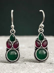 Close-up of oxidised silver green and red stone drop earrings against a dark teal background