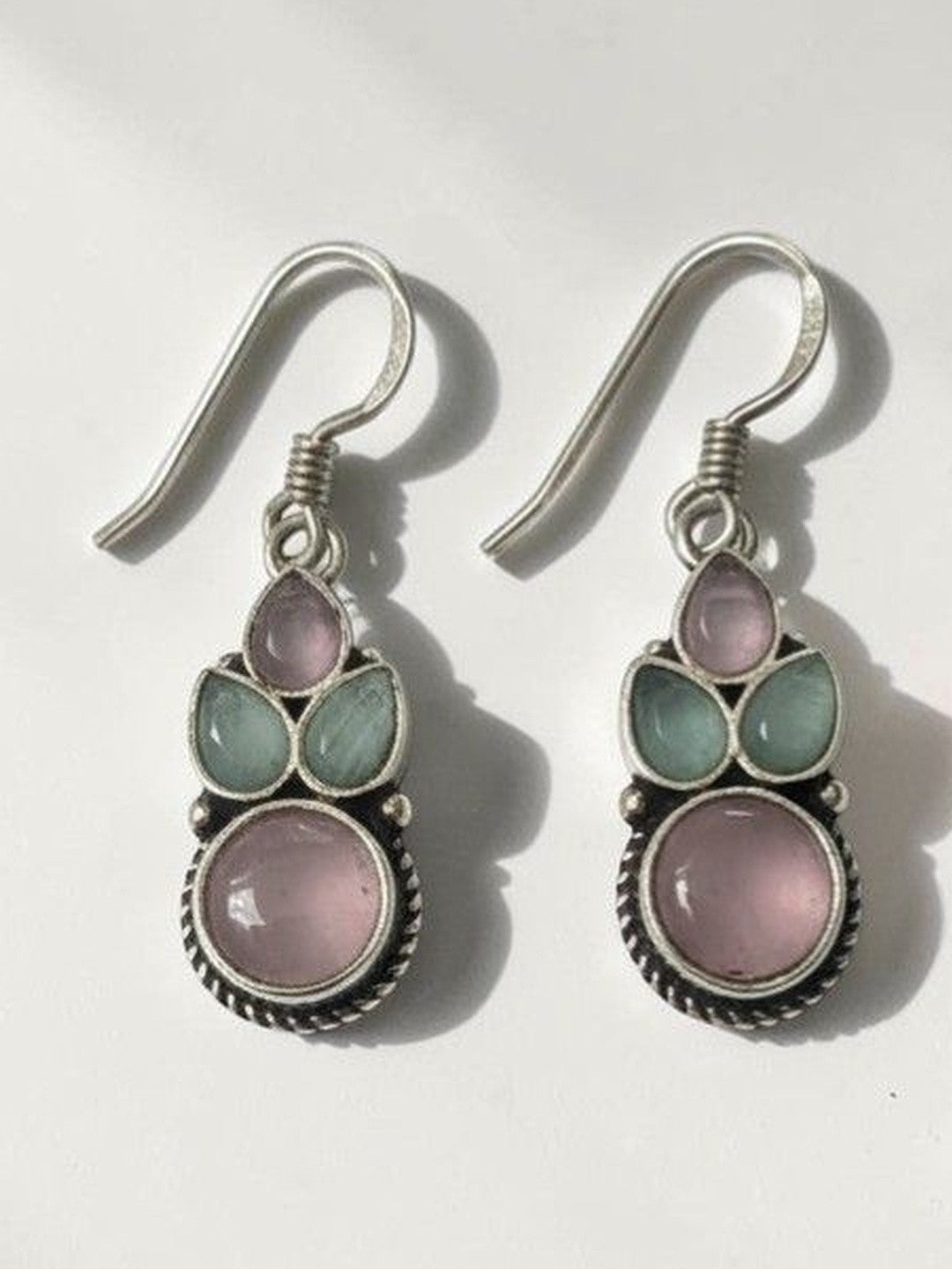 Pair of oxidised silver drop earrings with blush pink and sage green cabochon stones on white background