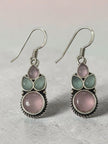 Close-up of oxidised silver hook earrings showing pink round stone and green leaf-shaped stones on grey surface