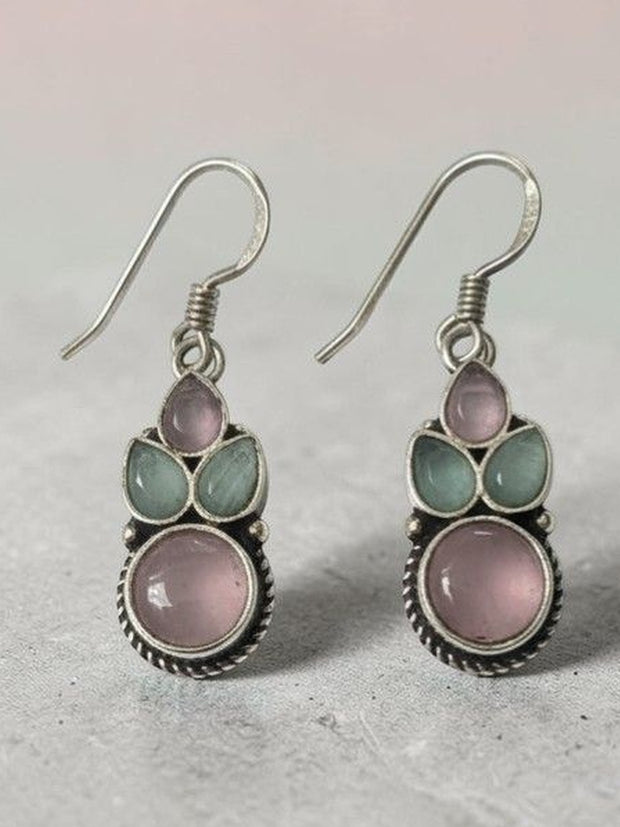 Close-up of oxidised silver hook earrings showing pink round stone and green leaf-shaped stones on grey surface
