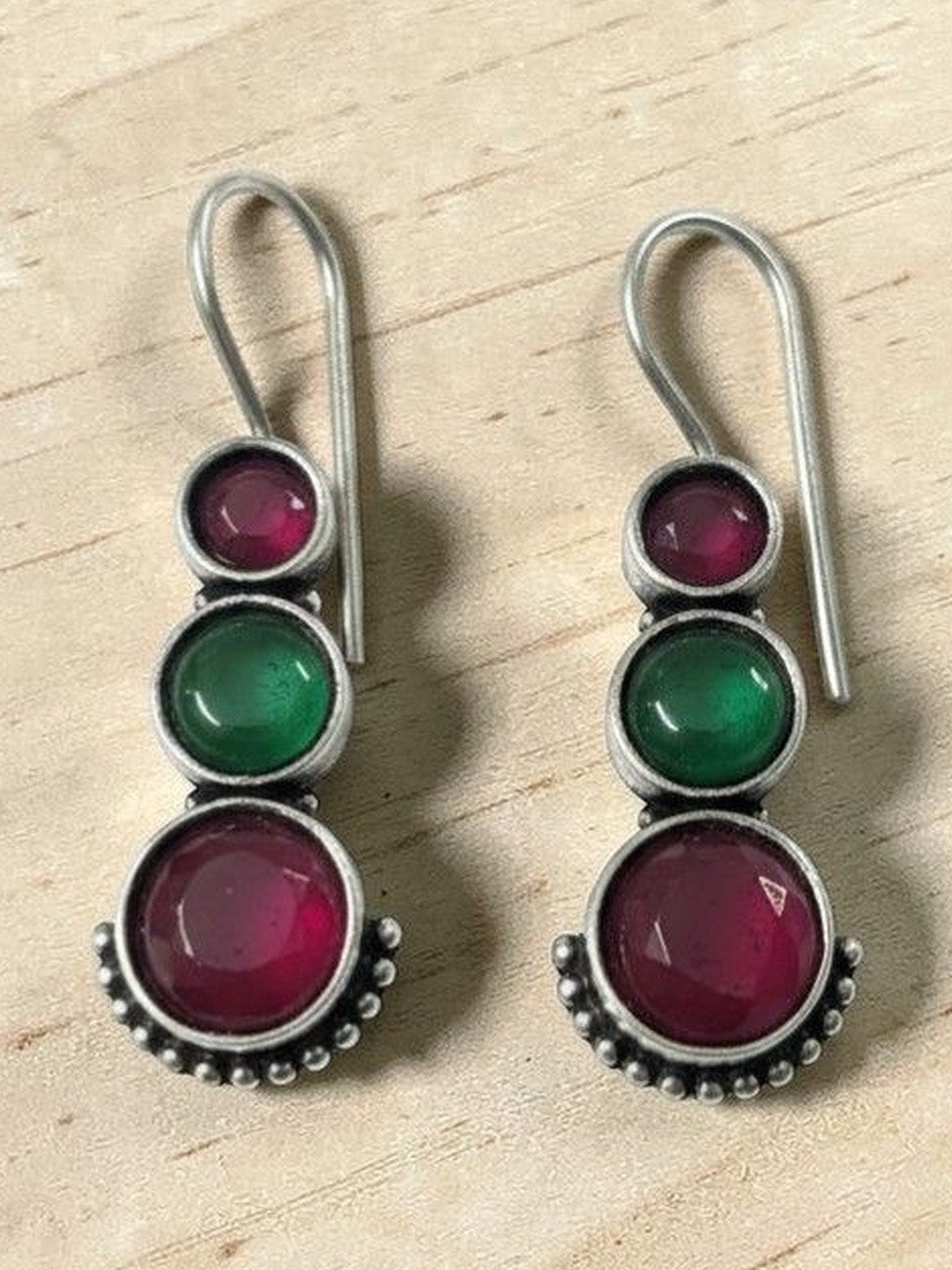 Pair of oxidised silver drop earrings with ruby-pink and green round stones on a wooden surface