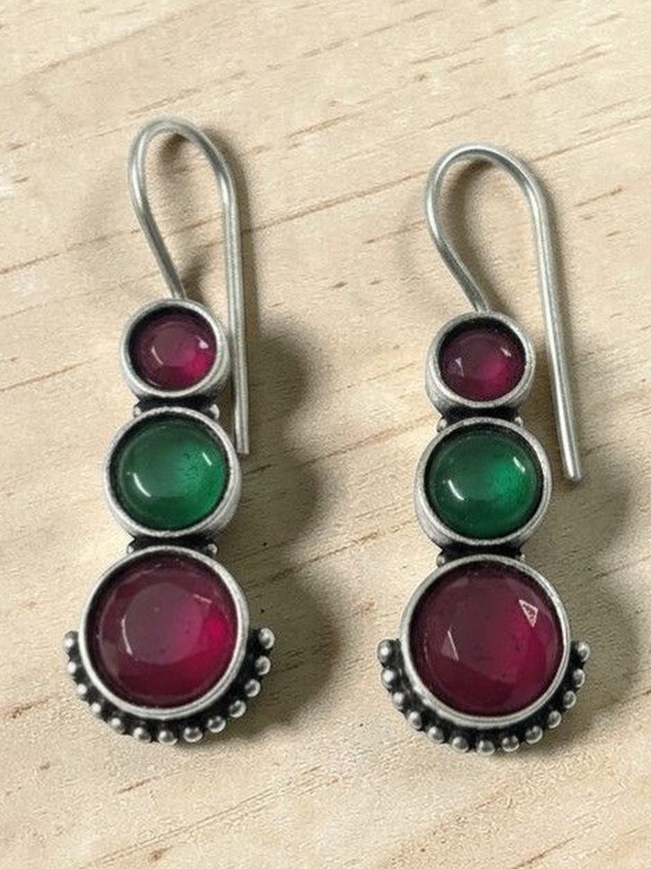 Pair of oxidised silver drop earrings with ruby-pink and green round stones on a wooden surface
