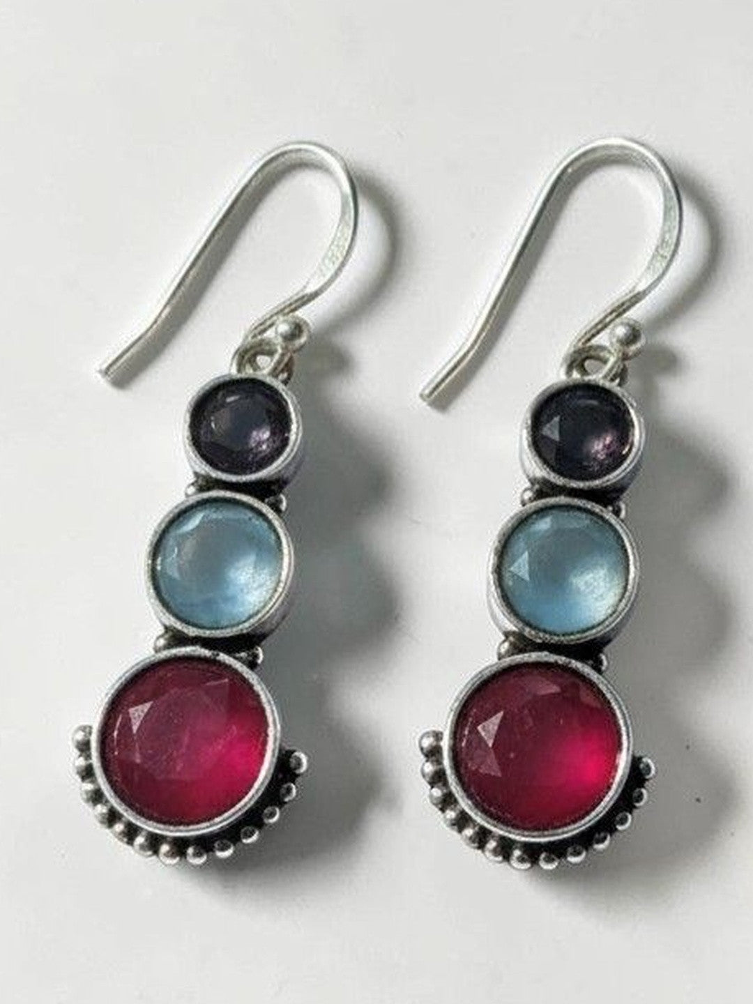Pair of oxidised silver drop earrings with indigo, blue, and ruby-pink round stones on a white background