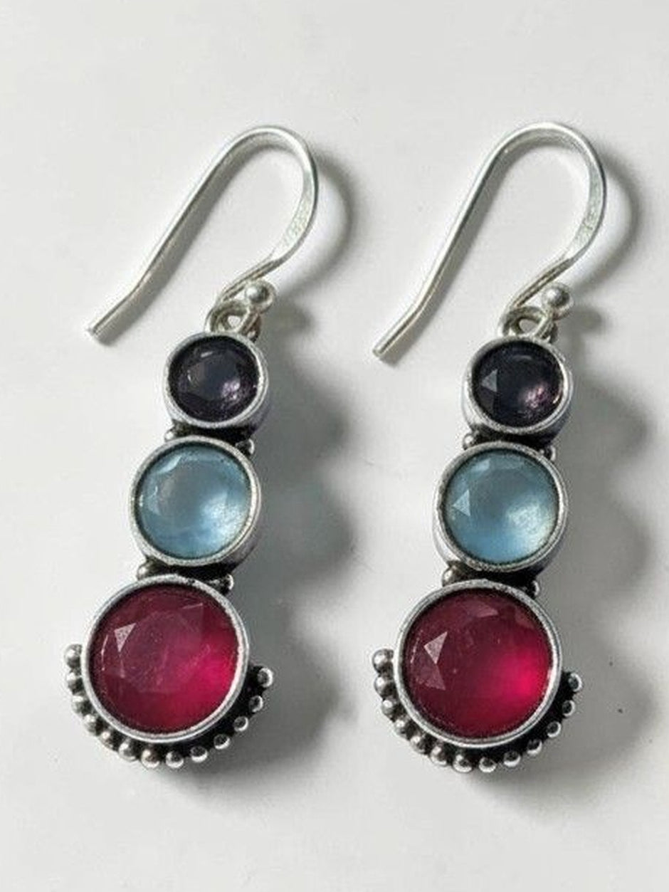 Pair of oxidised silver drop earrings with indigo, blue, and ruby-pink round stones on a white background