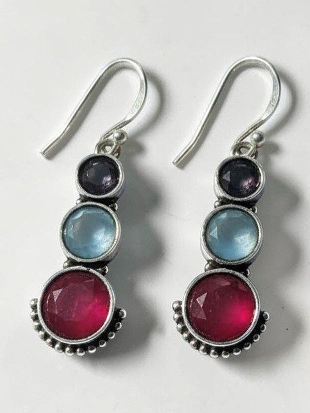 Pair of oxidised silver drop earrings with indigo, blue, and ruby-pink round stones on a white background