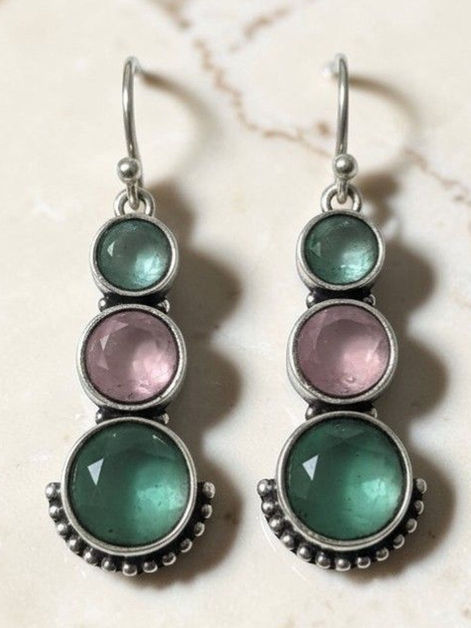 Pair of oxidised silver drop earrings with teal green and blush pink round stones on marble background