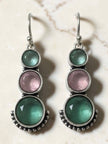 Pair of oxidised silver drop earrings with teal green and blush pink round stones on marble background