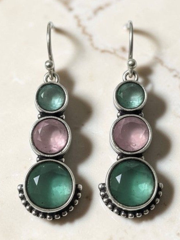 Pair of oxidised silver drop earrings with teal green and blush pink round stones on marble background