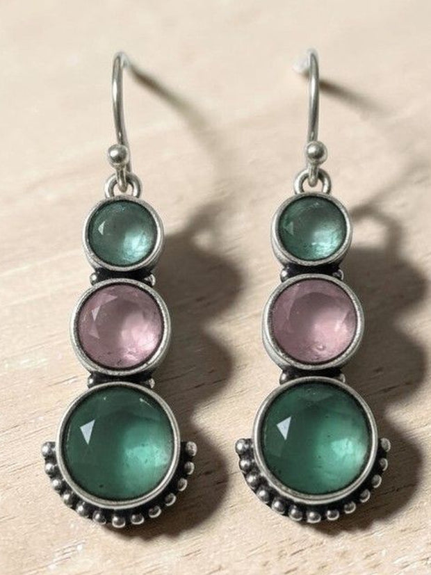 Oxidised silver three-stone drop earrings with green and pink stones displayed on wooden surface